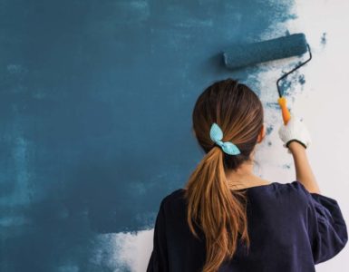 woman with brown hair in ponytail painting a wall with paint roller