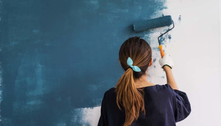 woman with brown hair in ponytail painting a wall with paint roller
