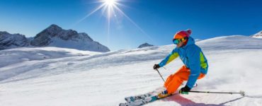 person in a blue coat and orange pants skiing down the mountain under a bright sun